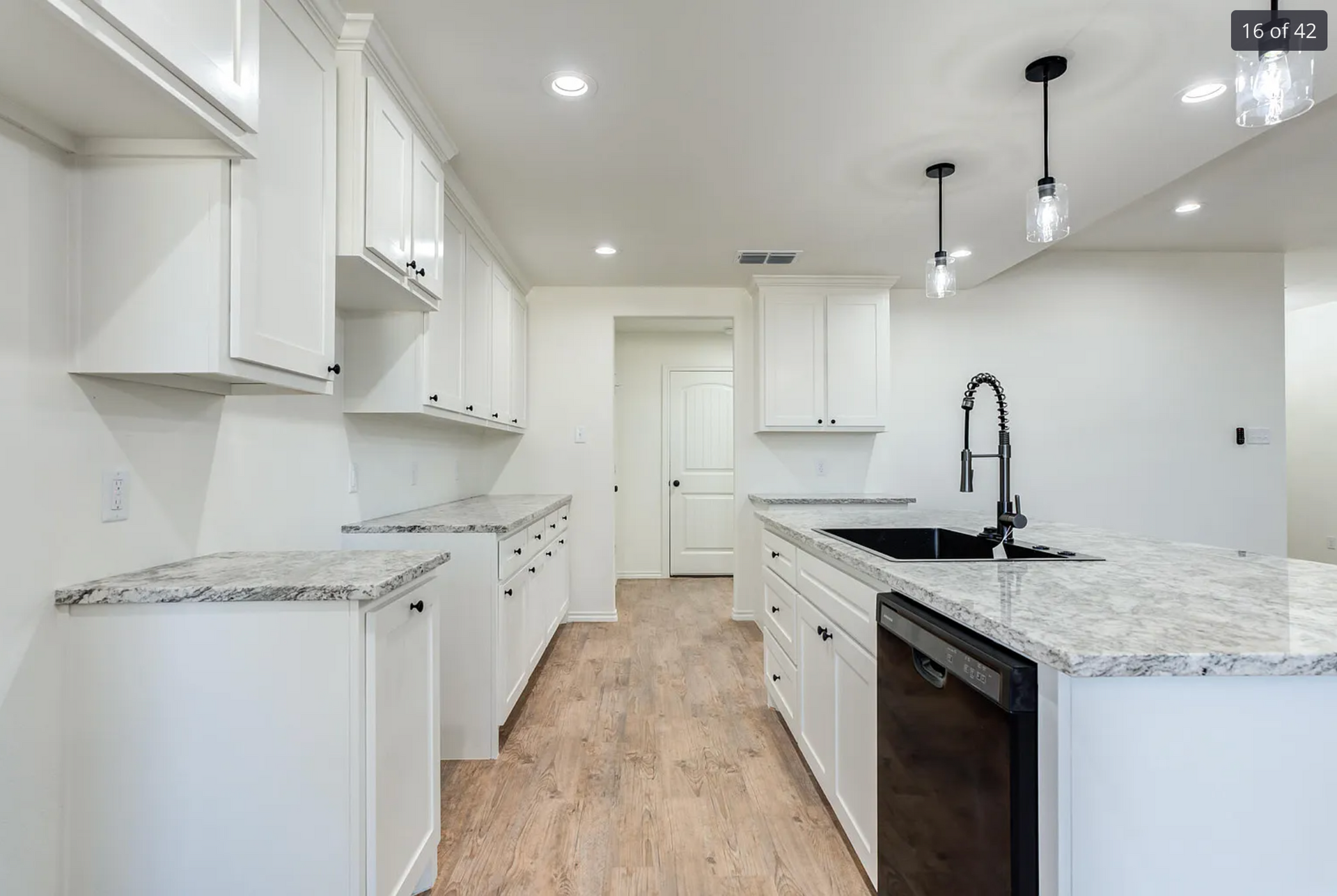 White kitchen with island, cabinets, granite countertops, and black faucet.