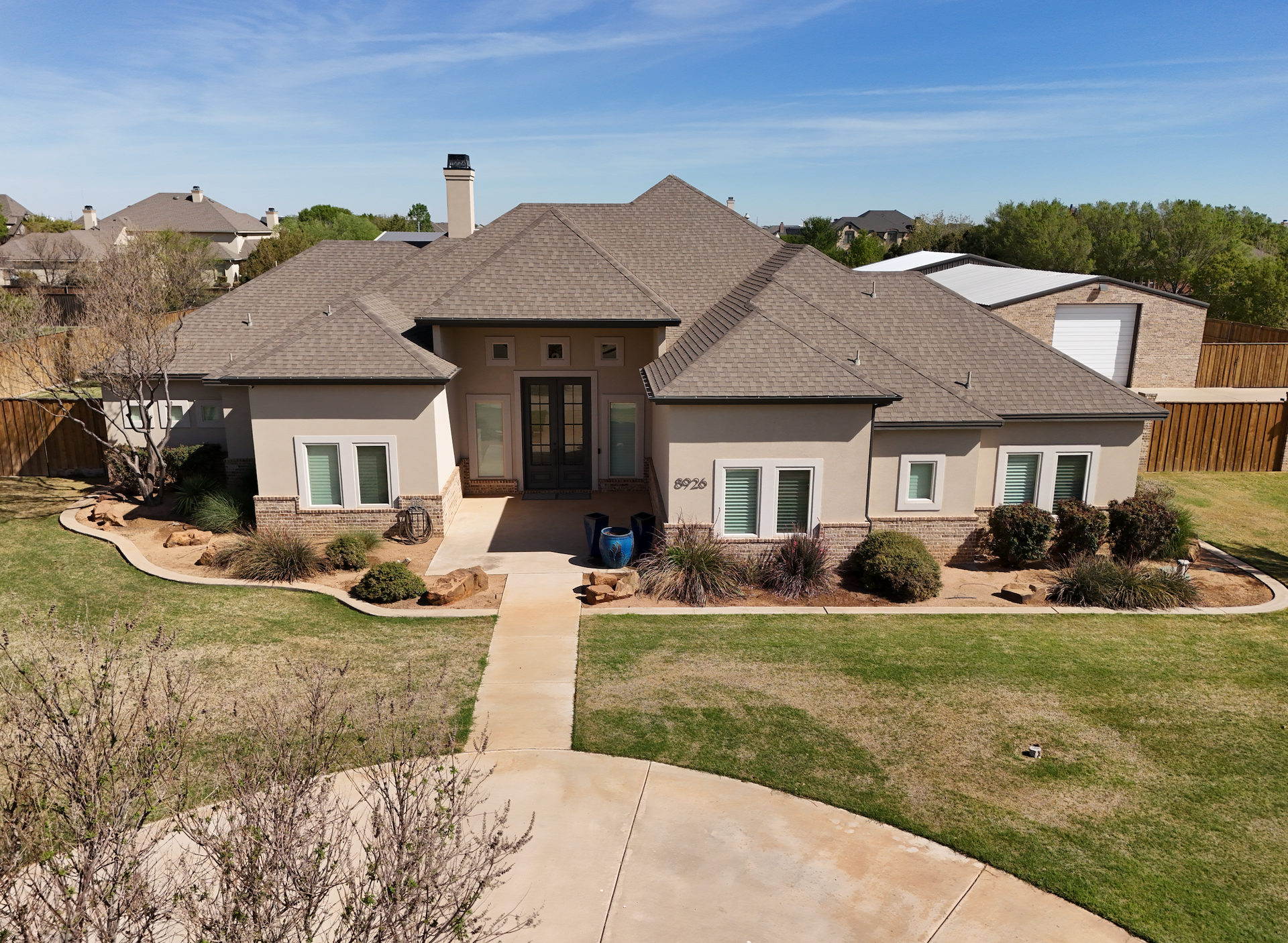 Front view of a tan suburban house with a tiled roof, walkway, and landscaped yard