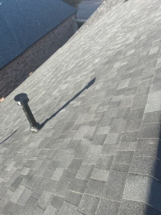 Gray shingle roof with black vent pipe; the long shadow of the pipe is cast on the roof.