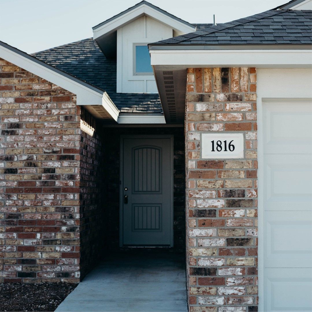 Brick house exterior with a door, dormer, and garage door; house number 1816.