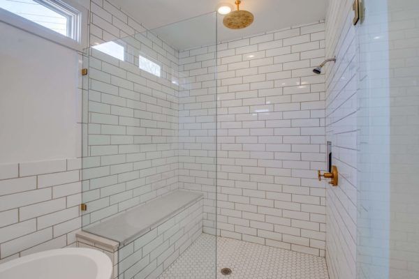 Modern white tiled bathroom with a glass shower enclosure and a built-in bench.