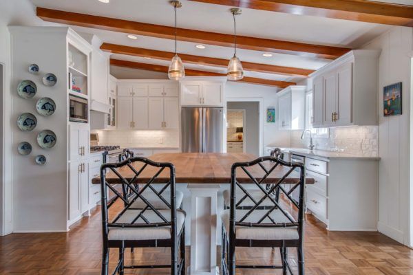 Bright white kitchen with a wooden island, wooden beams, and pendant lights.