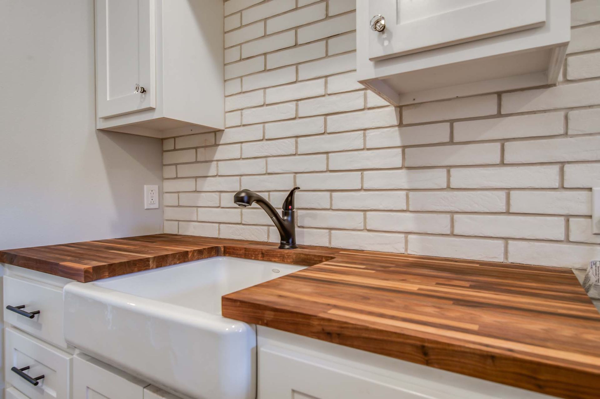 Kitchen with white cabinets, farmhouse sink, wood countertops, and brick-style backsplash.