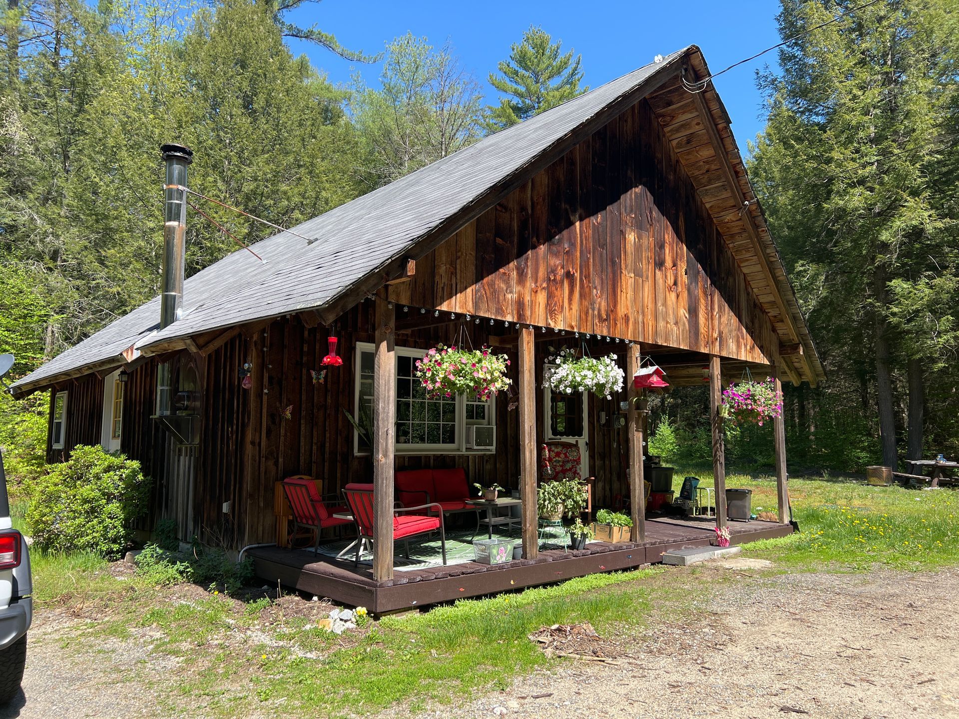 A small wooden cabin with a porch and a car parked in front of it.