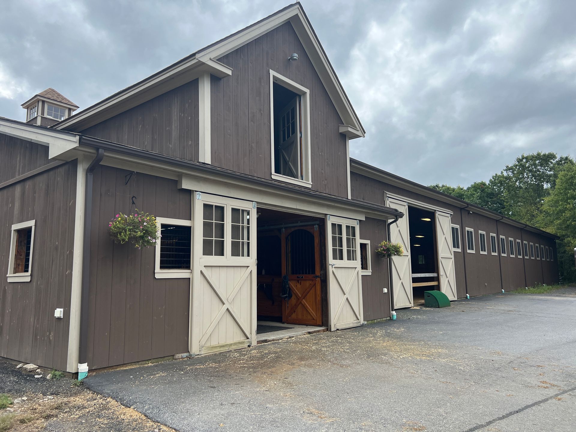 A brown and white barn with a white door is sitting on top of a gravel road.