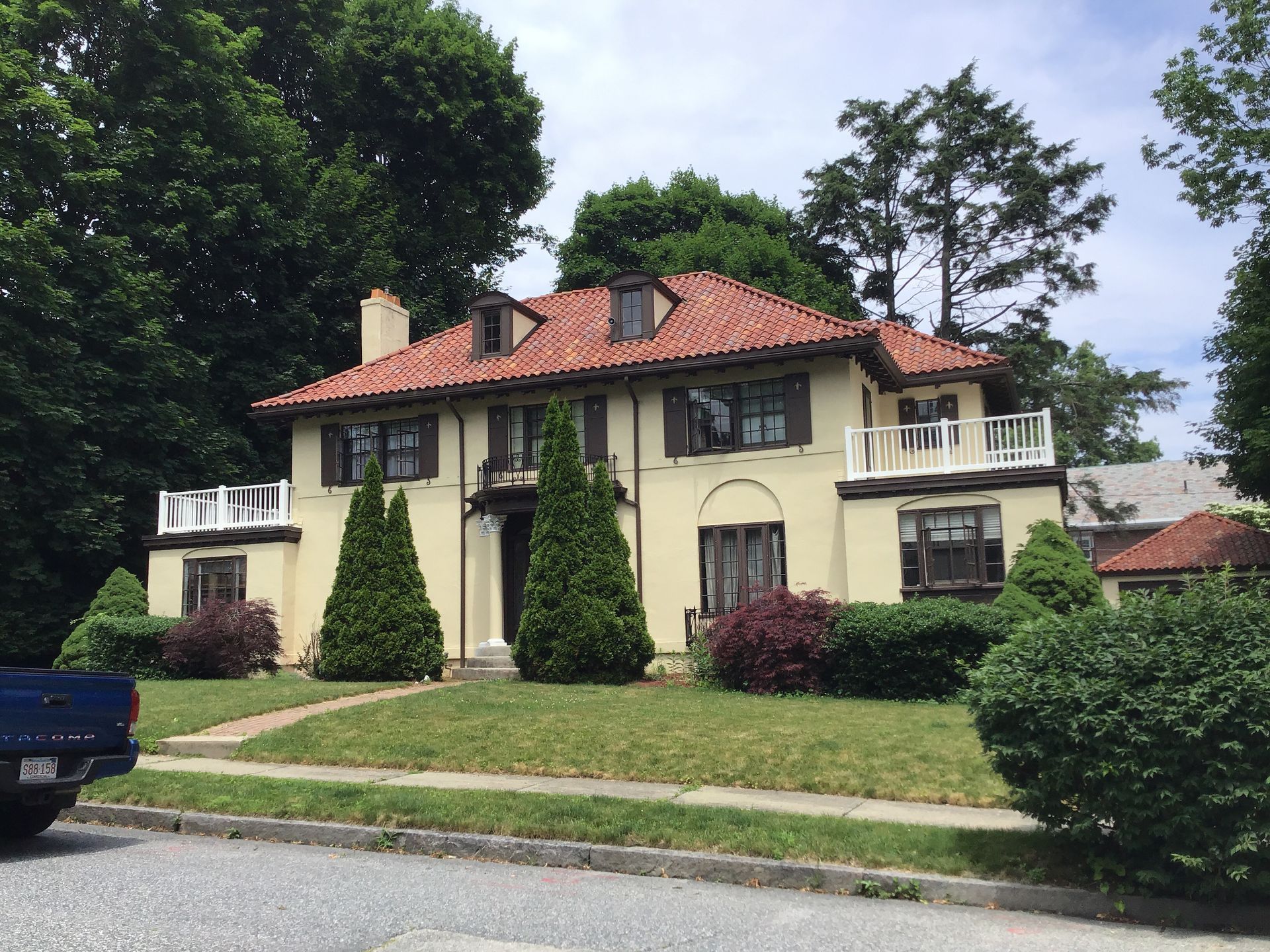 A yellow house with a red tile roof and a blue truck parked in front of it