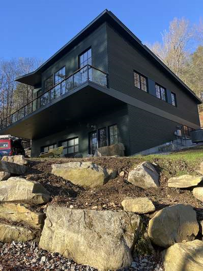 A large black house is sitting on top of a rocky hill.