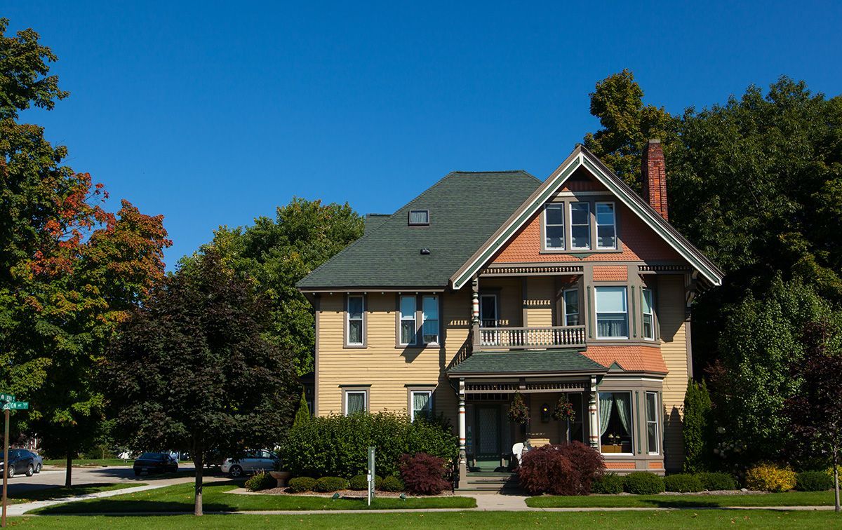 A large house with a green roof is surrounded by trees on a sunny day.