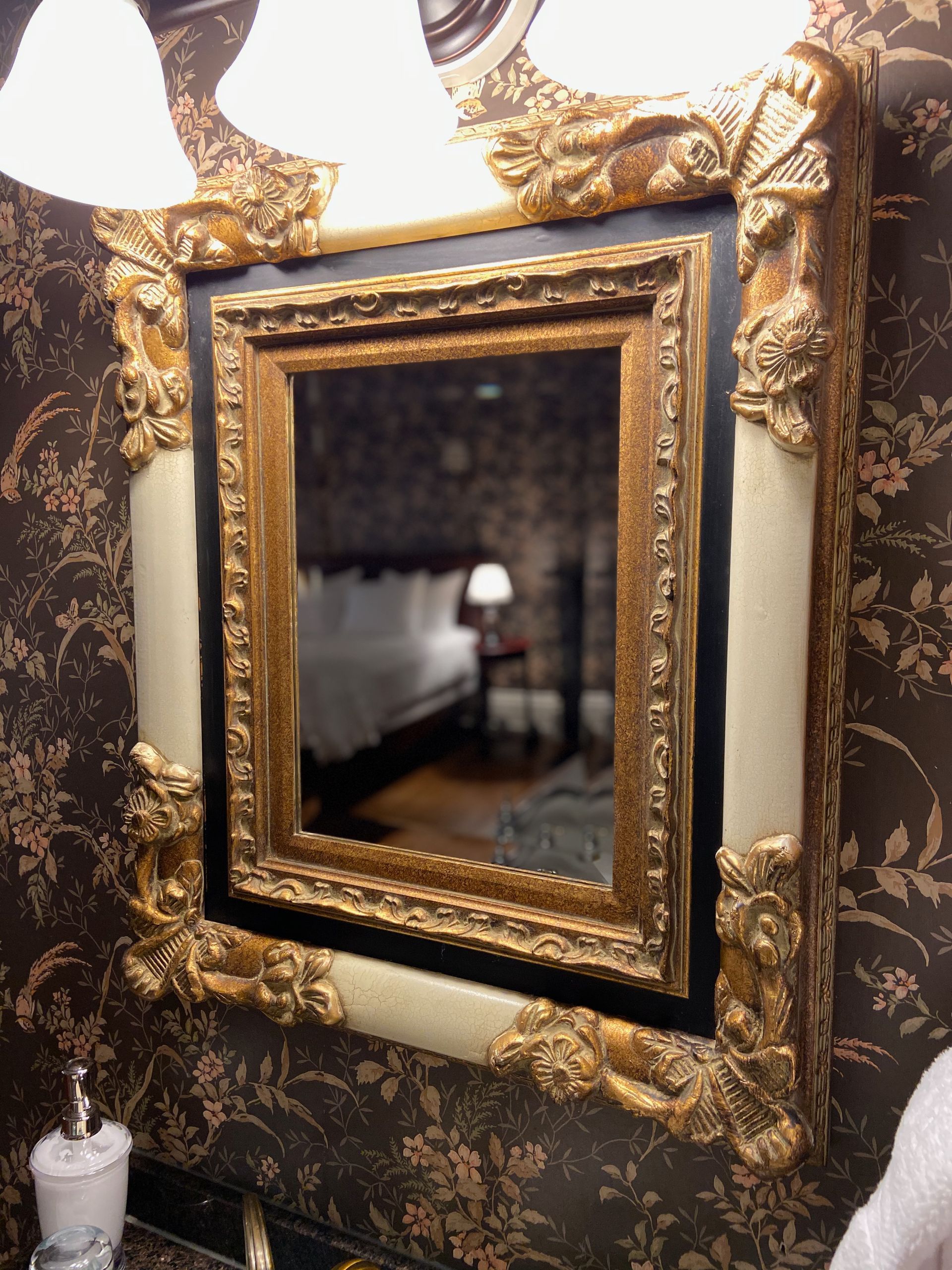 A bathroom mirror with a gold and white frame