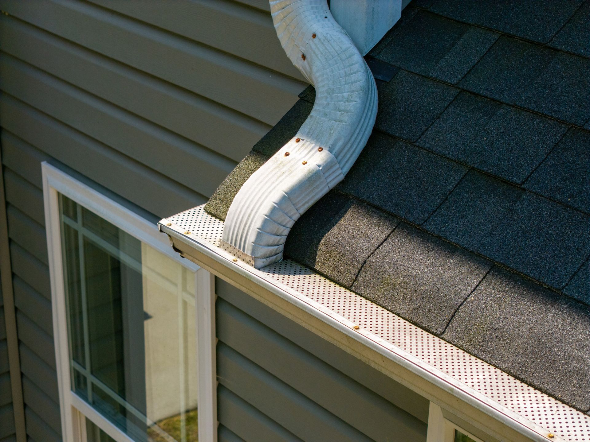 A gutter on the side of a house next to a window