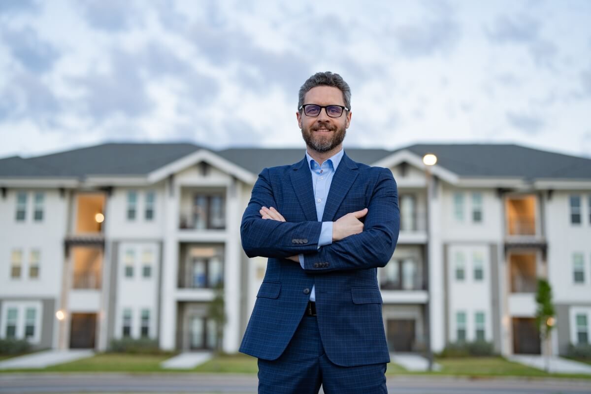 Smiling property manager standing in front of apartment complex he manages

