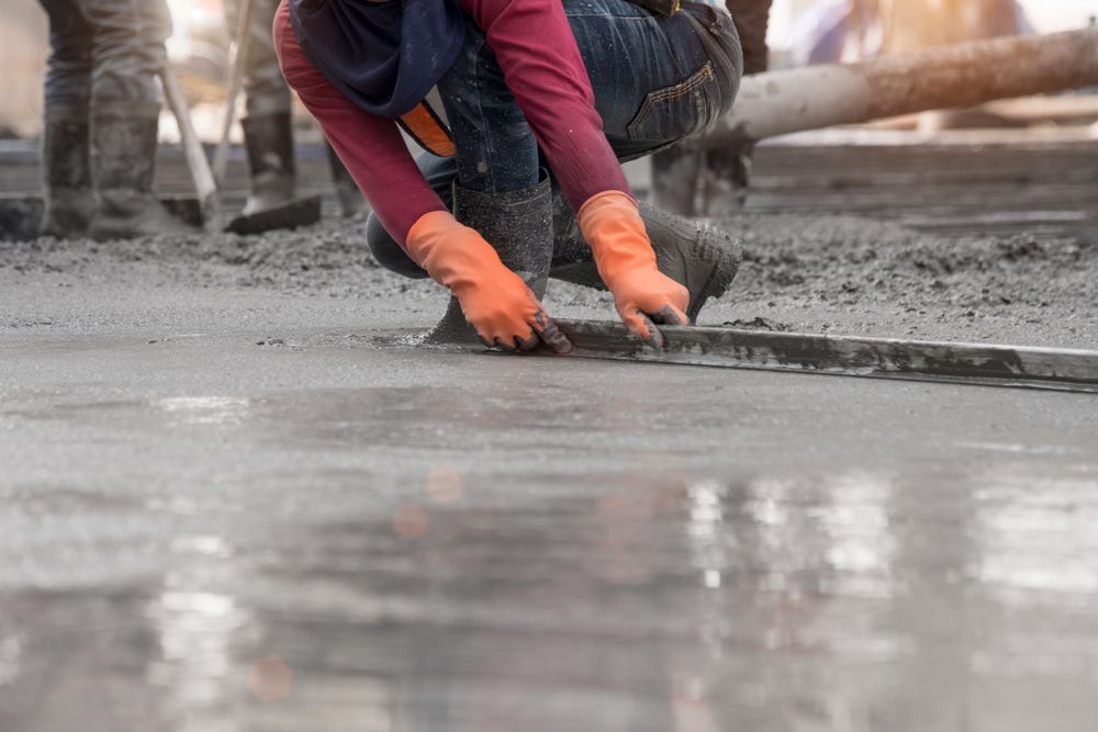 A Construction Worker Is Kneeling Down And Spreading Concrete On The Ground — Tiger Concrete ACT In Fadden, ACT