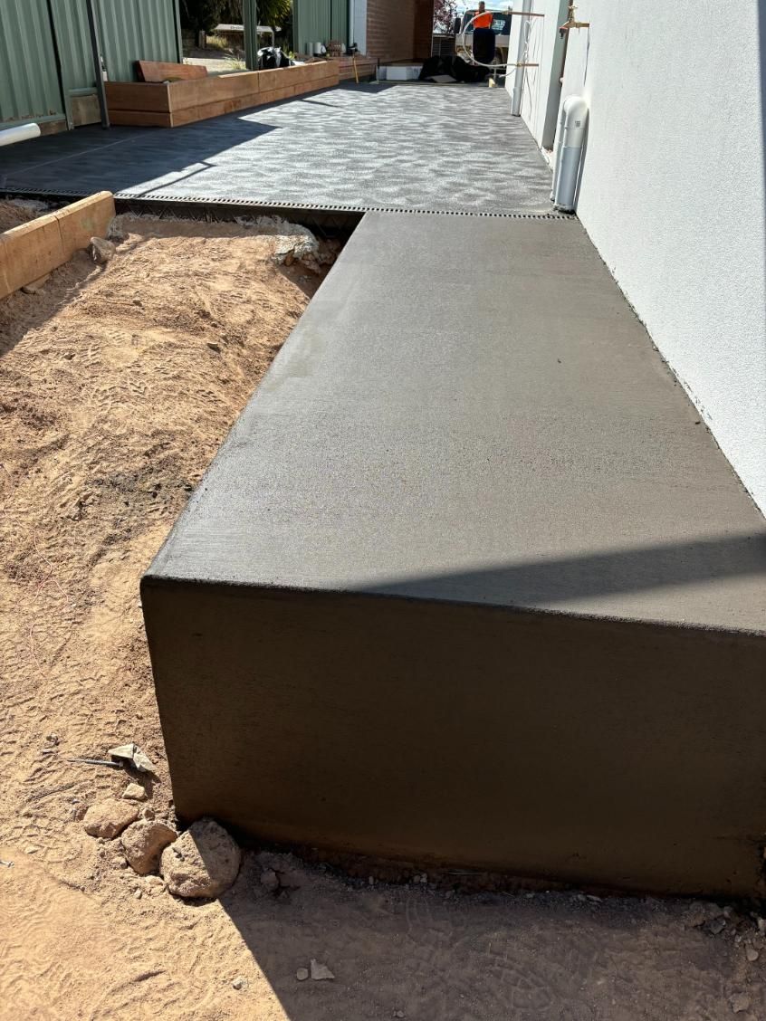 A Concrete Bench Is Sitting In The Dirt Next To A Building — Tiger Concrete ACT In Fadden, ACT