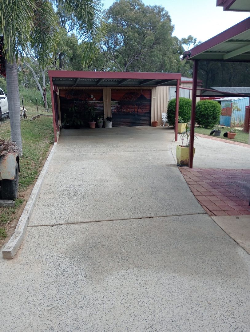 Driveway leading to a carport with a red roof; trees and greenery in the background.