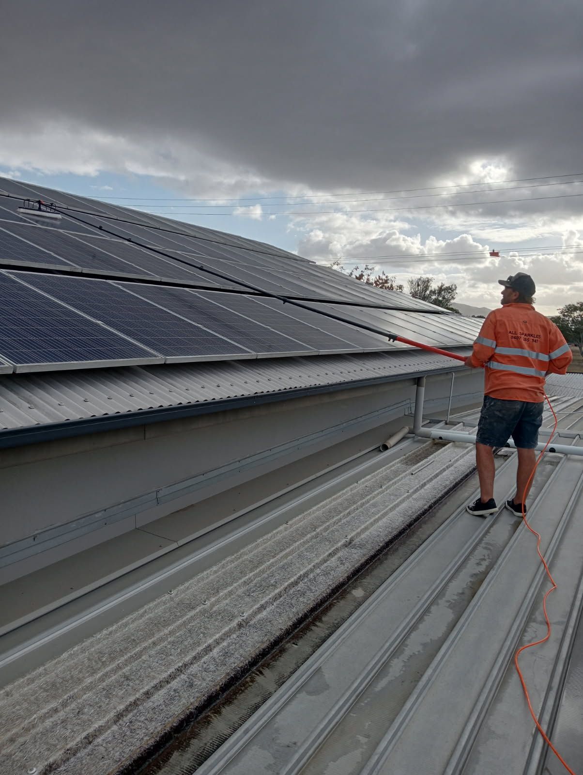 Man Cleaning Solar Panels on a Metal Roof — All Sparkles Cleaning Technology In Bowen, QLD