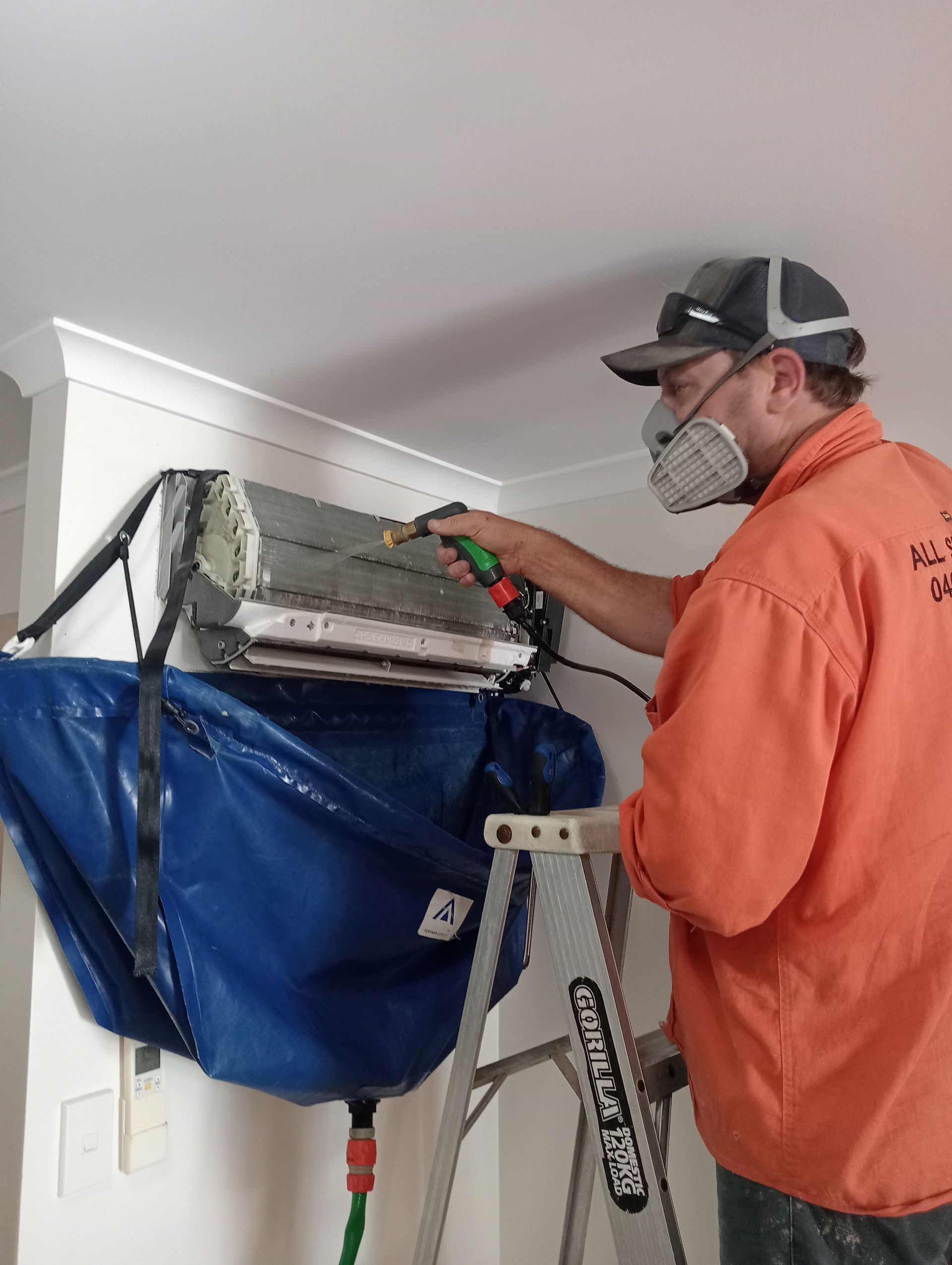 Man Cleaning a Wall-mounted Air Conditioner Unit on a Ladder — All Sparkles Cleaning Technology In Collinsville, QLD
