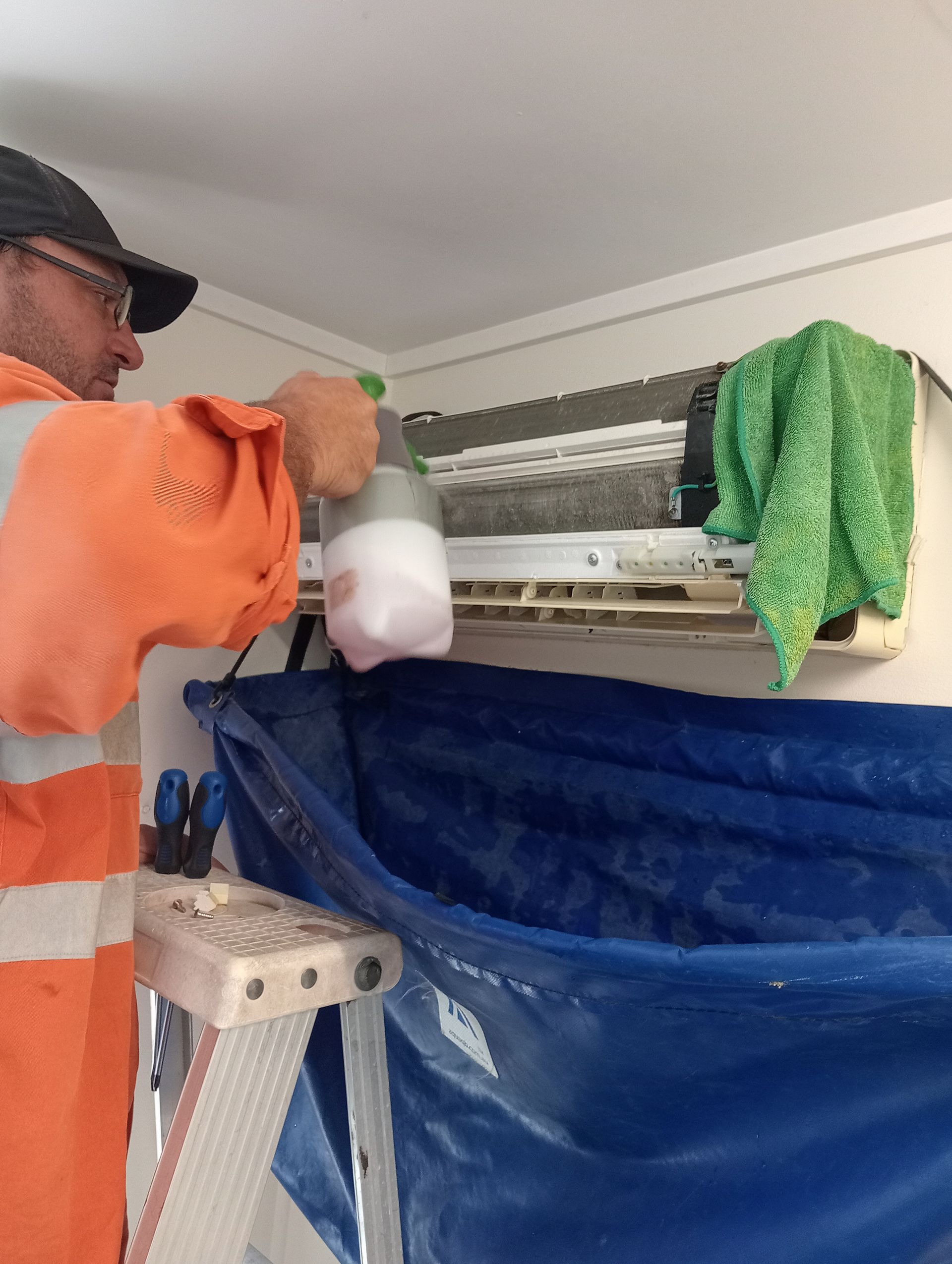 Person Spraying an Air Conditioner With a Solution — All Sparkles Cleaning Technology In Proserpine, QLD
