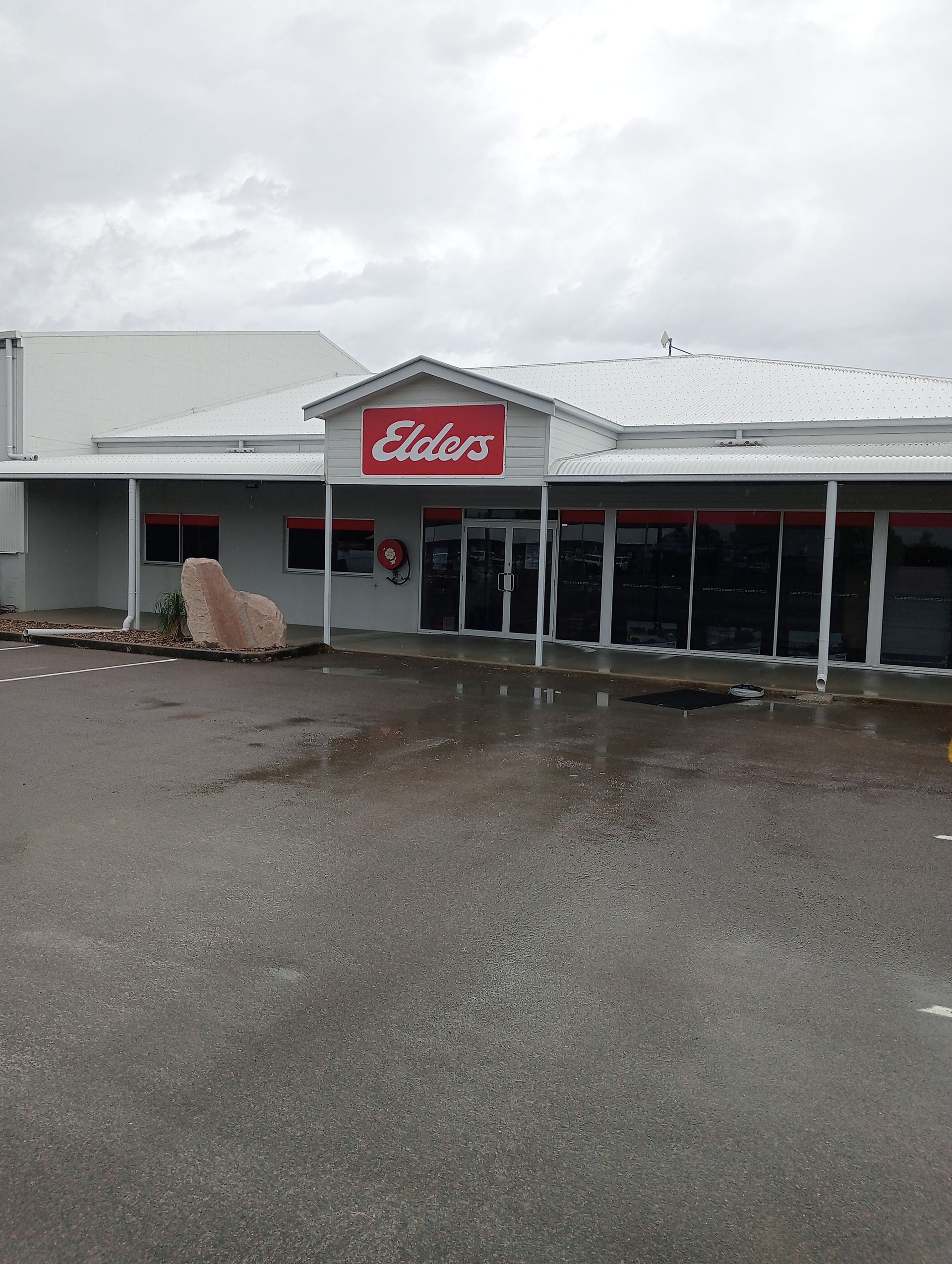 Elders Real Estate Building With Red Sign, Glass Windows, and Wet Pavement — All Sparkles Cleaning Technology In Bowen, QLD