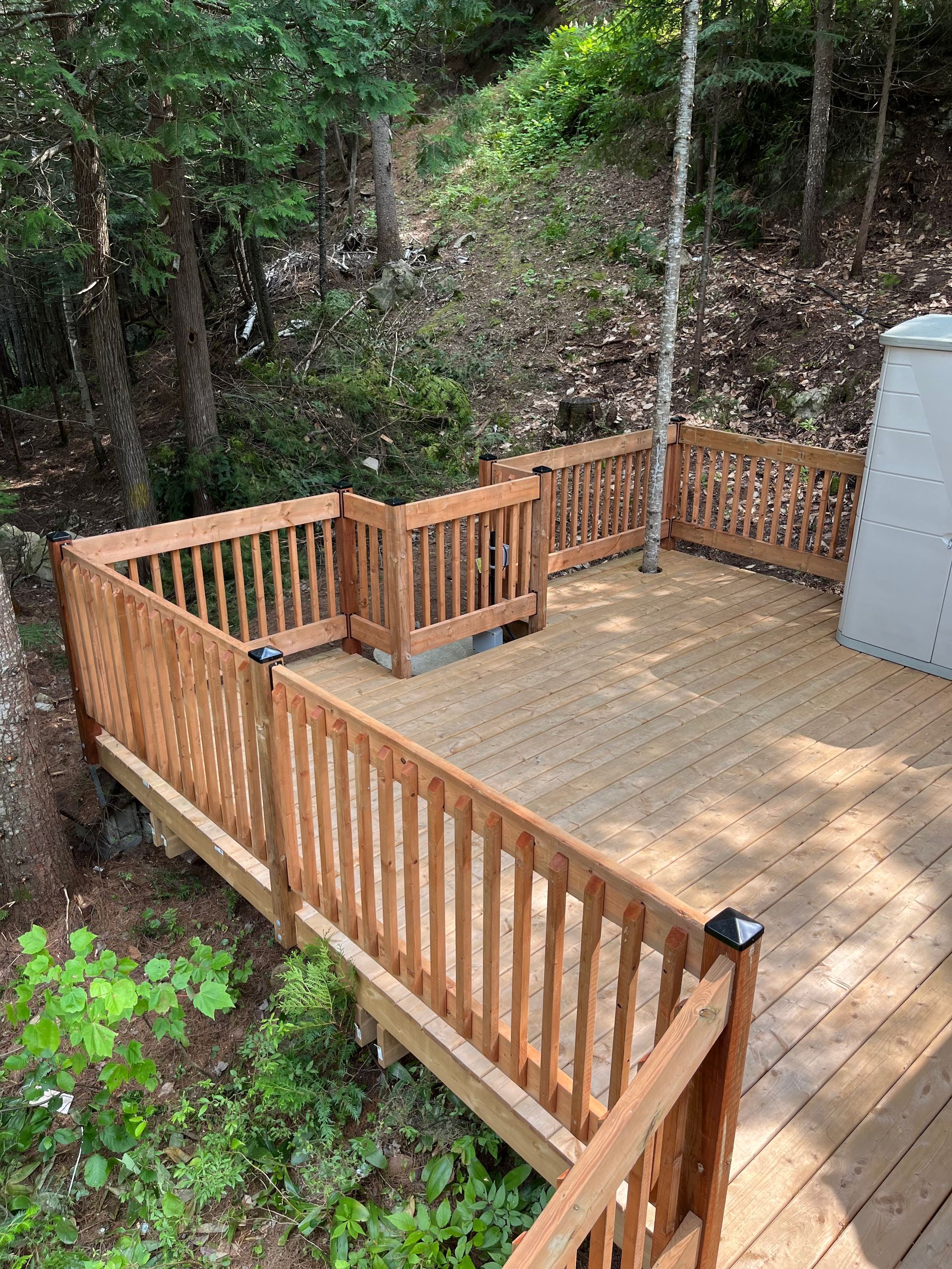 Une terrasse en bois entourée d'une clôture est entourée d'arbres.