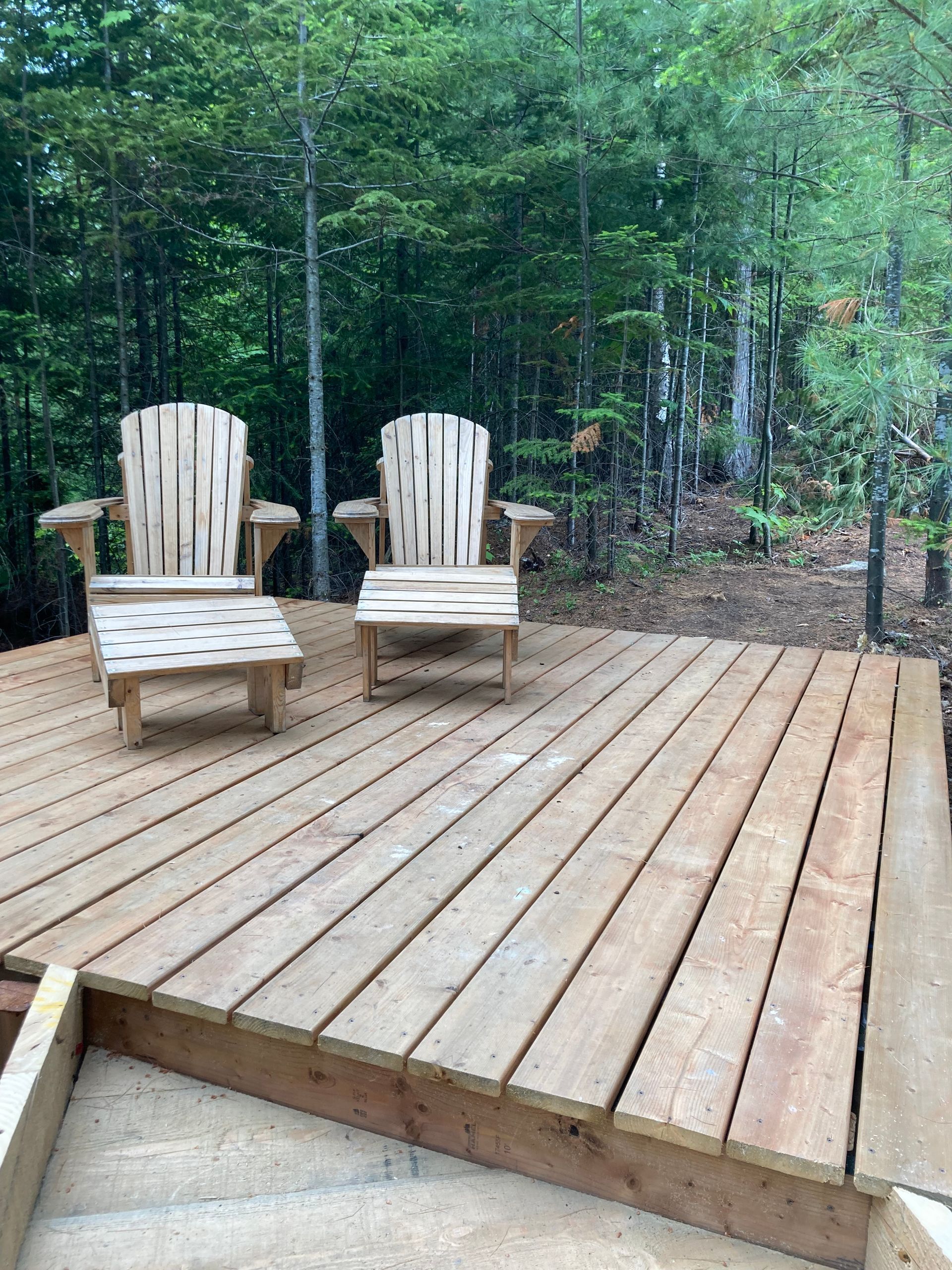 Deux chaises en bois sont assises sur une terrasse en bois dans les bois.