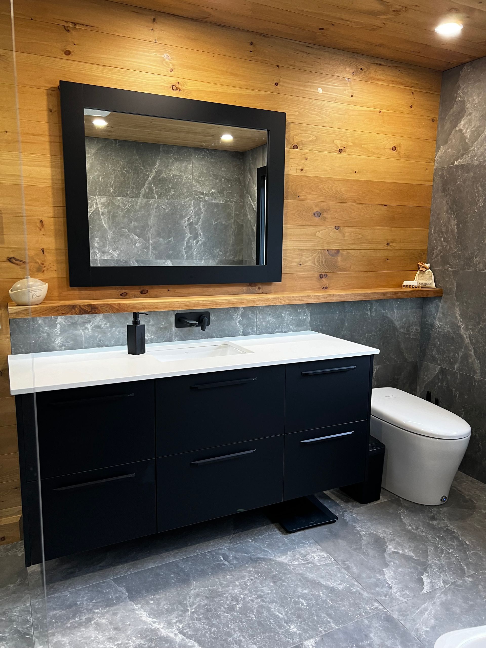 Une salle de bain avec lavabo, WC, miroir et murs en bois.