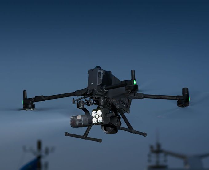 Black drone with camera gimbal on landing gear, parked on a road at sunset.