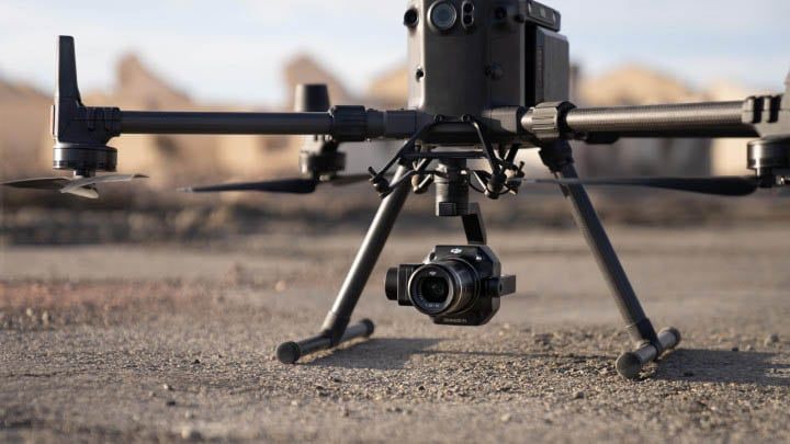 A person operates a drone remote controller during sunset, with a flying drone in the blurred background.
