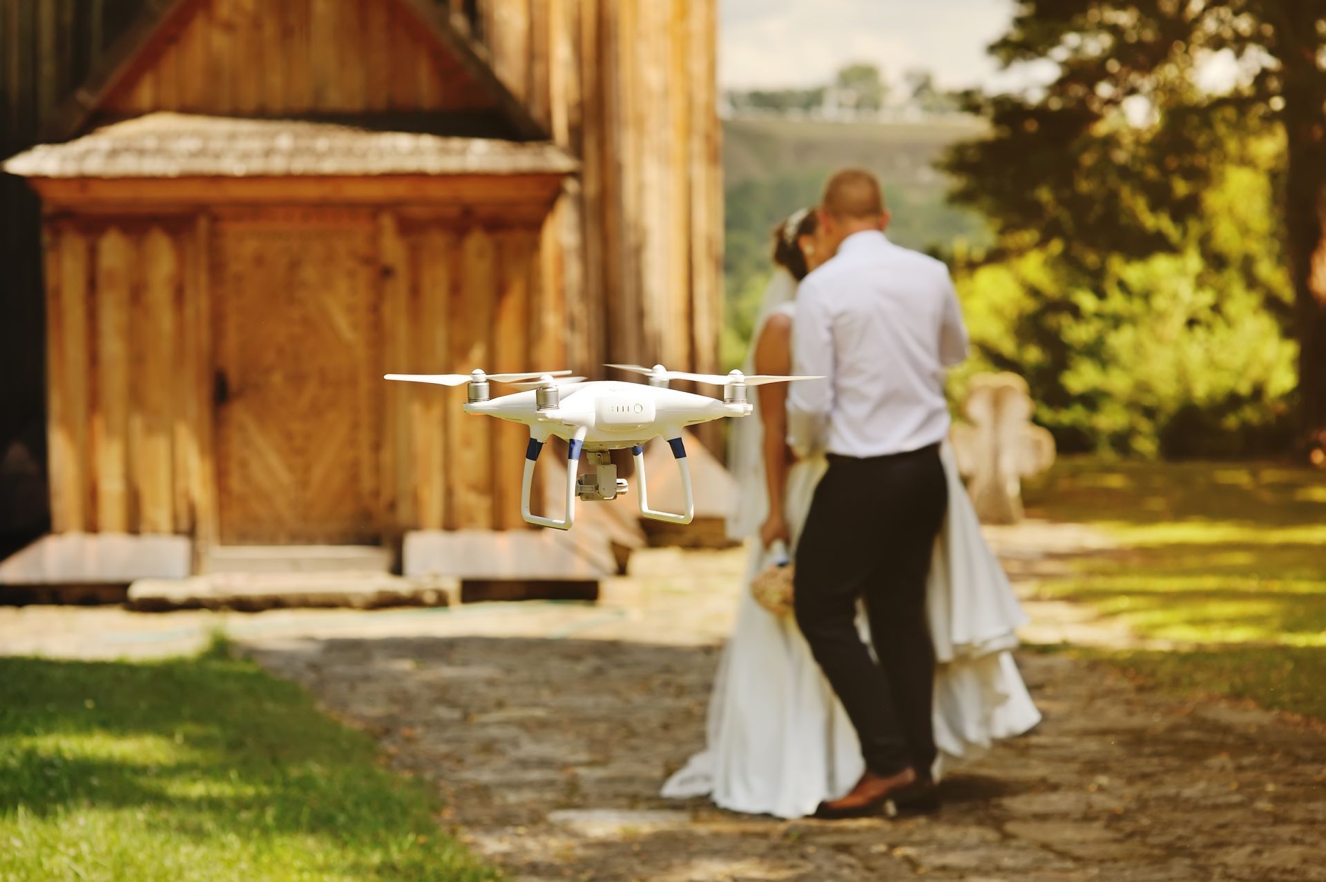 A person operates a drone remote controller during sunset, with a flying drone in the blurred background.