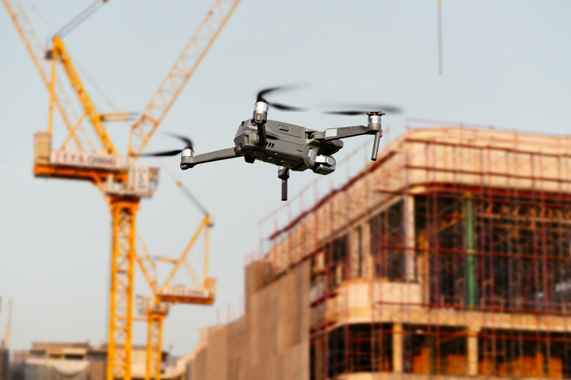A drone flies over a city at twilight, shining a bright spotlight down onto the buildings below.