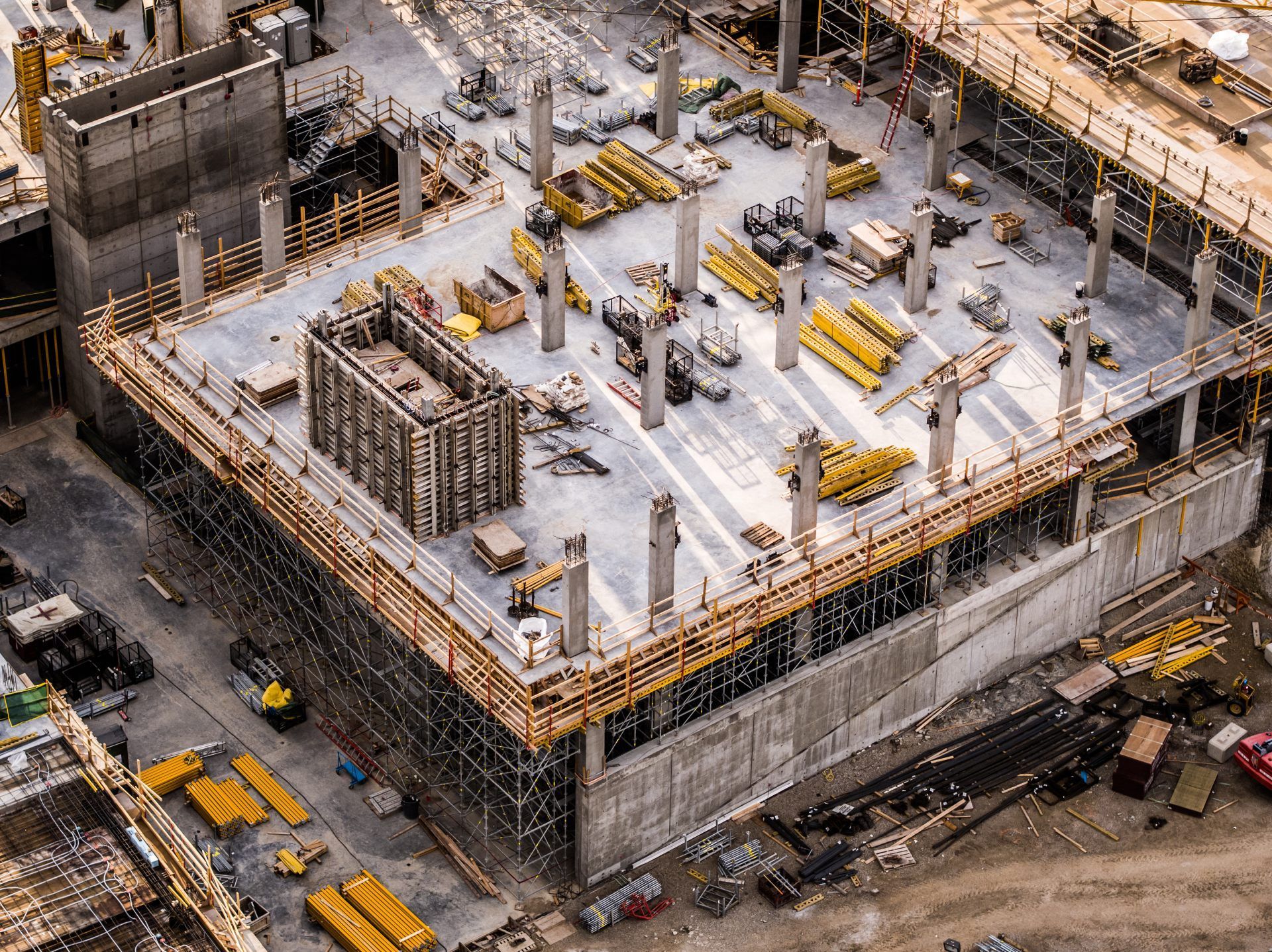 Aerial view of a concrete building under construction with cranes, scaffolding, and workers on site