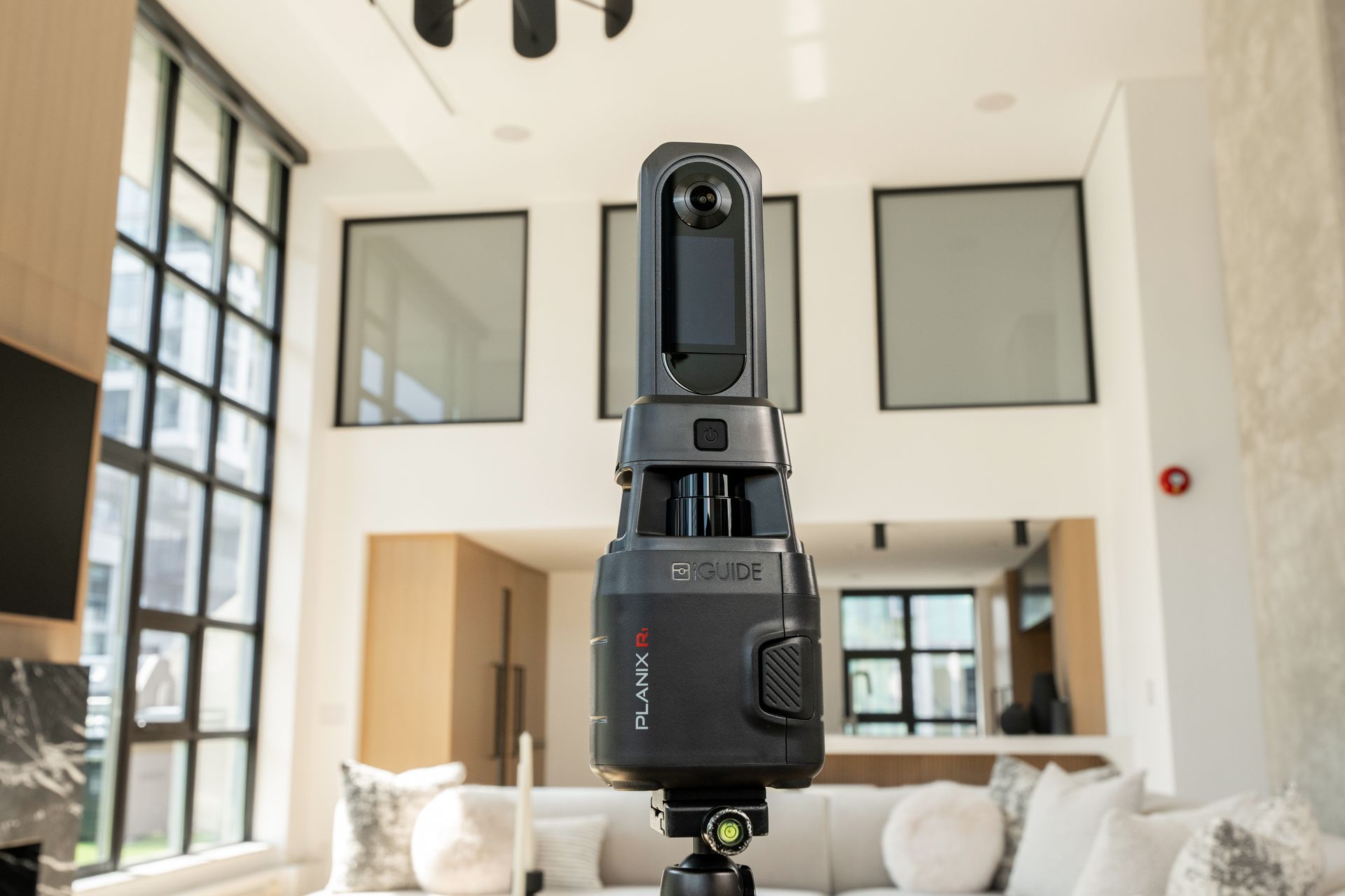 Black 360-degree camera mounted in a bright modern living room with high ceilings and large windows