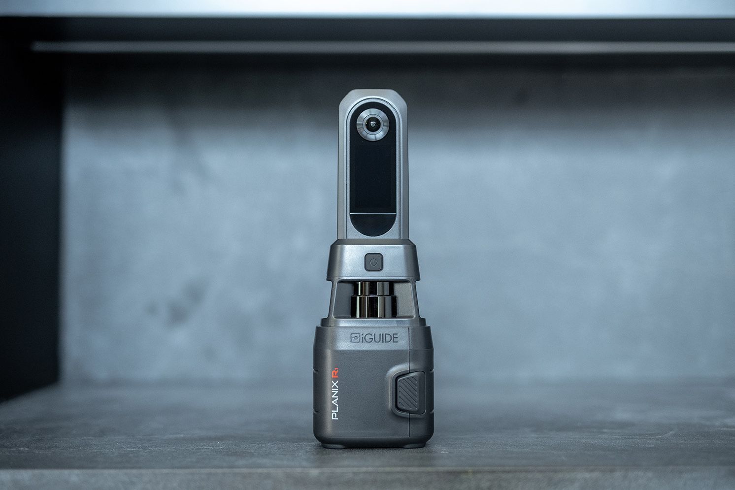 Small gray handheld device with a vertical display, standing upright on a table.