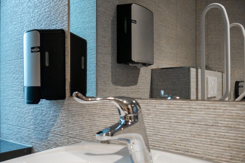 Een wastafel met zeepdispenser en spiegel.