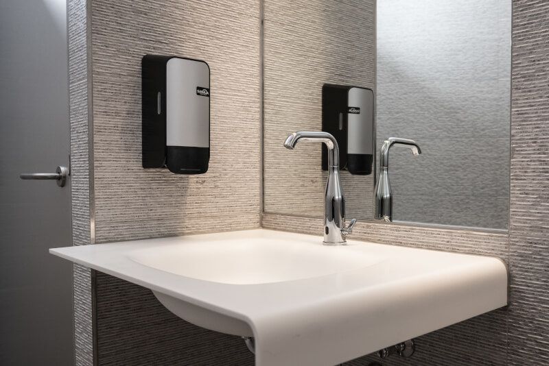 Een wastafel met spiegel en zeepdispensers aan de muur.