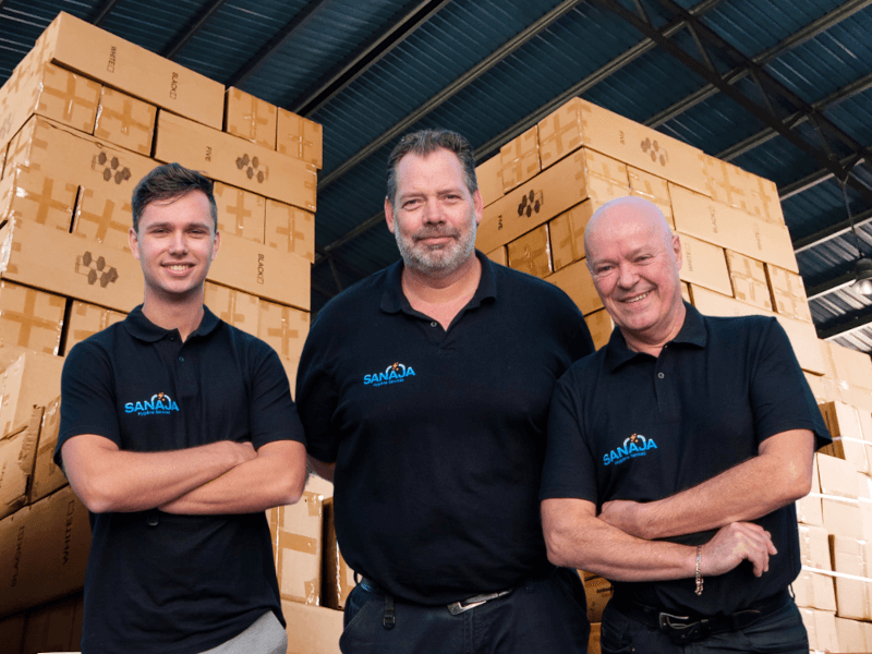 Drie mannen poseren voor een foto voor een stapel dozen.