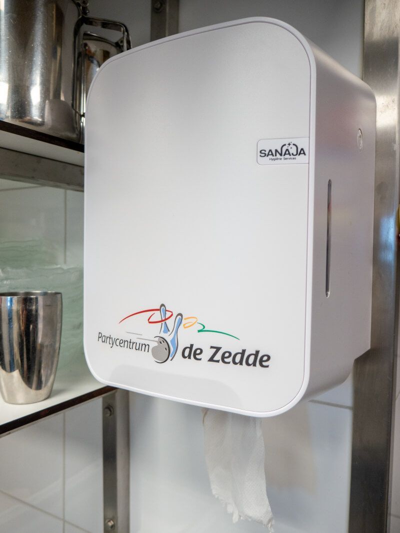 Een witte dispenser voor papieren handdoeken hangt aan de muur in een keuken.