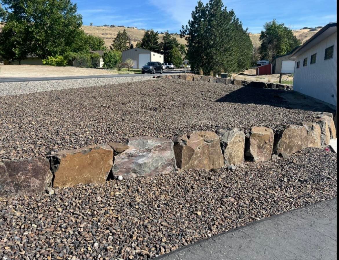 Gravel driveway with a rock border, blue sky, and surrounding buildings.