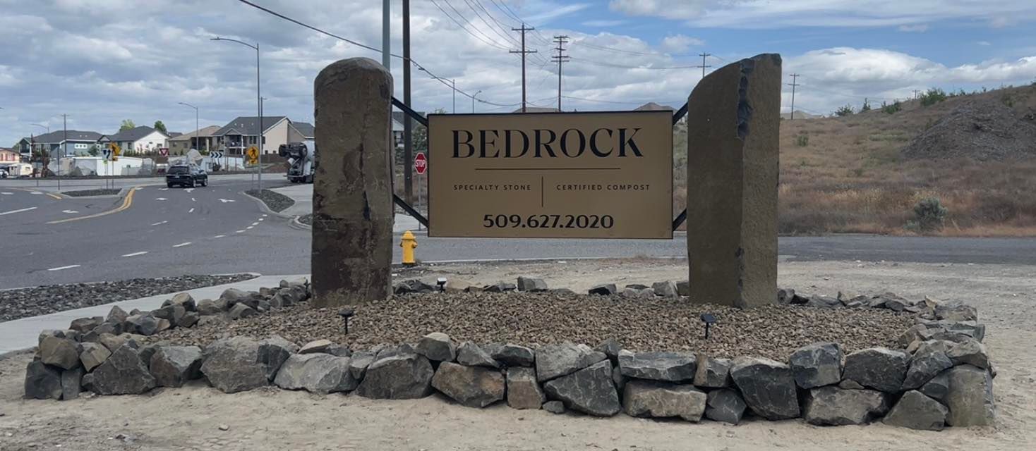 Woman in straw hat smiles, holding wine glass near a lake.