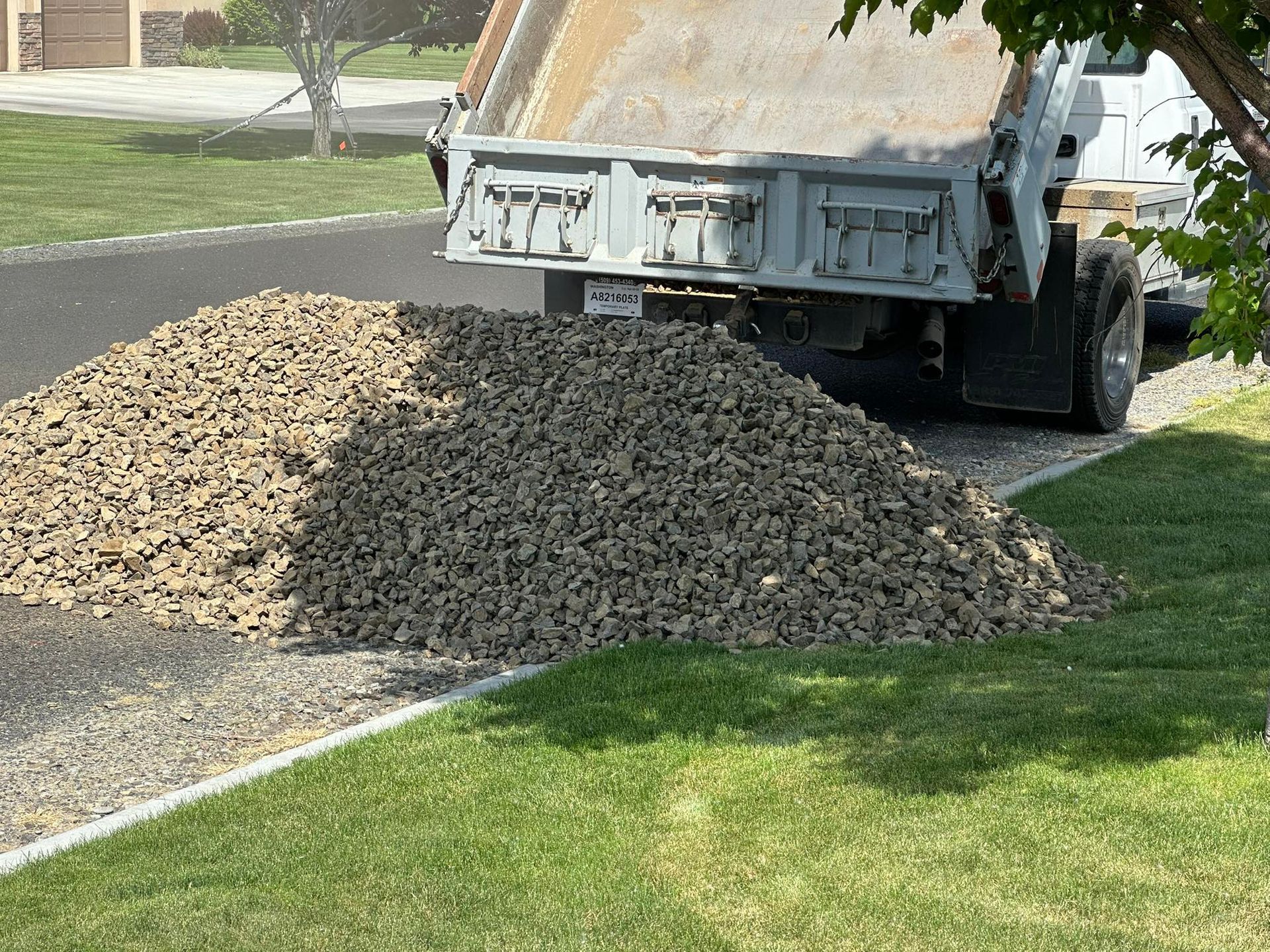 Truck bed dumping gravel onto a driveway next to a lawn.