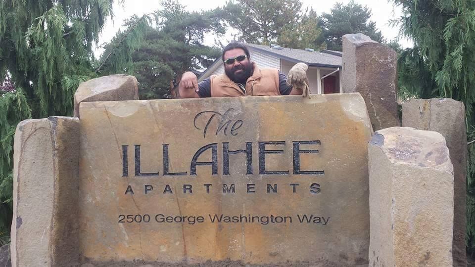 Woman in straw hat smiles, holding wine glass near a lake.