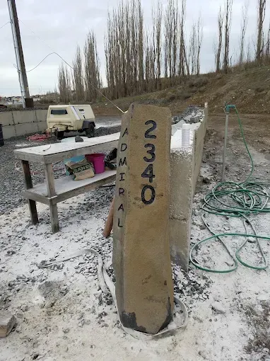 Concrete pillar with the address 2340 Admiral painted on it. A table, trailer, and trees are in the background.