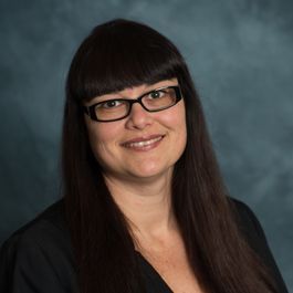 A woman wearing glasses and a black jacket is smiling for the camera.