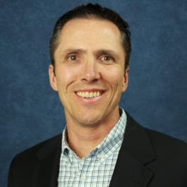 A man in a suit and plaid shirt is smiling for the camera