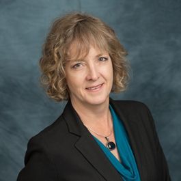 A woman in a black jacket and blue shirt is smiling for the camera.