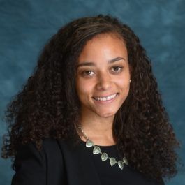 A woman with curly hair is wearing a black shirt and a necklace.