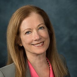 A woman in a suit and pink shirt is smiling for the camera.