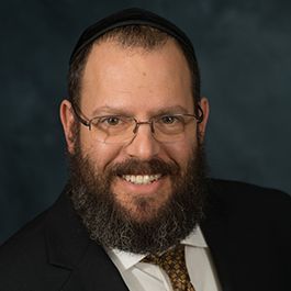 A man with a beard and glasses is wearing a suit and tie and smiling.