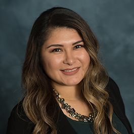 A woman wearing a necklace and a black jacket is smiling for the camera.