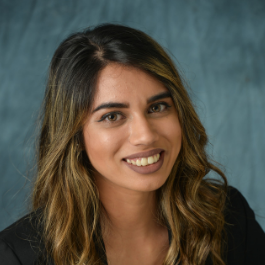 A woman with long hair is smiling and wearing a black jacket.