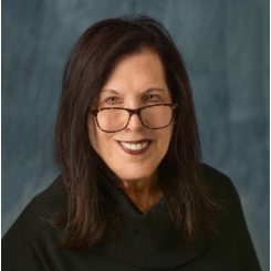 A woman wearing glasses and a black sweater is smiling for the camera.